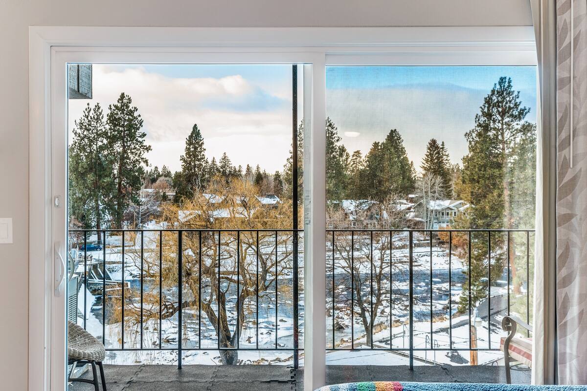 A room with a large sliding glass door leading to a balcony with a view of a snowy landscape and trees.
