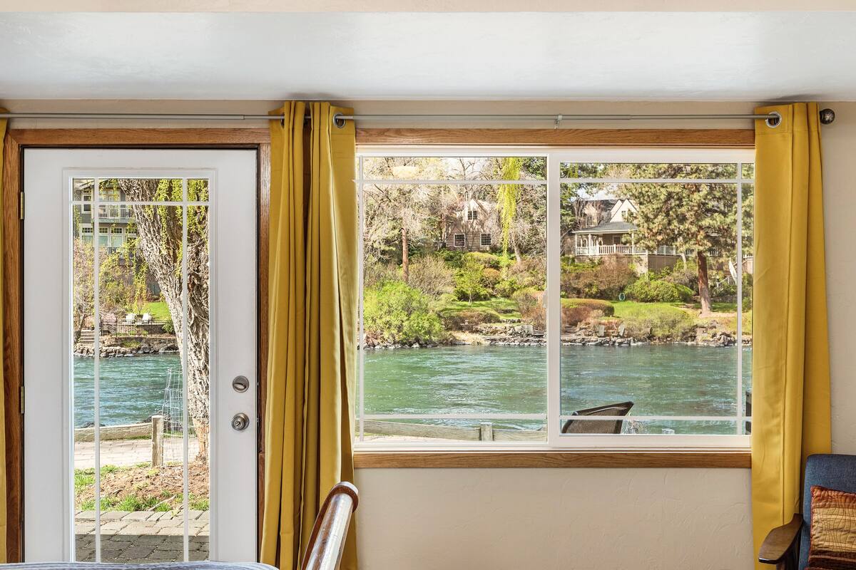 A room with a view of a river, a door, and a window with yellow curtains.