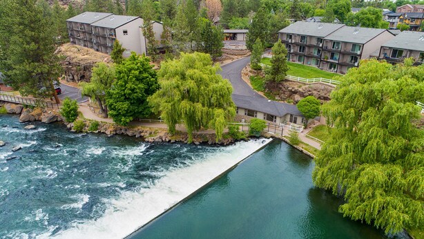 Un río serpentea por una zona residencial con modernos edificios de apartamentos, un puente y abundante vegetación.