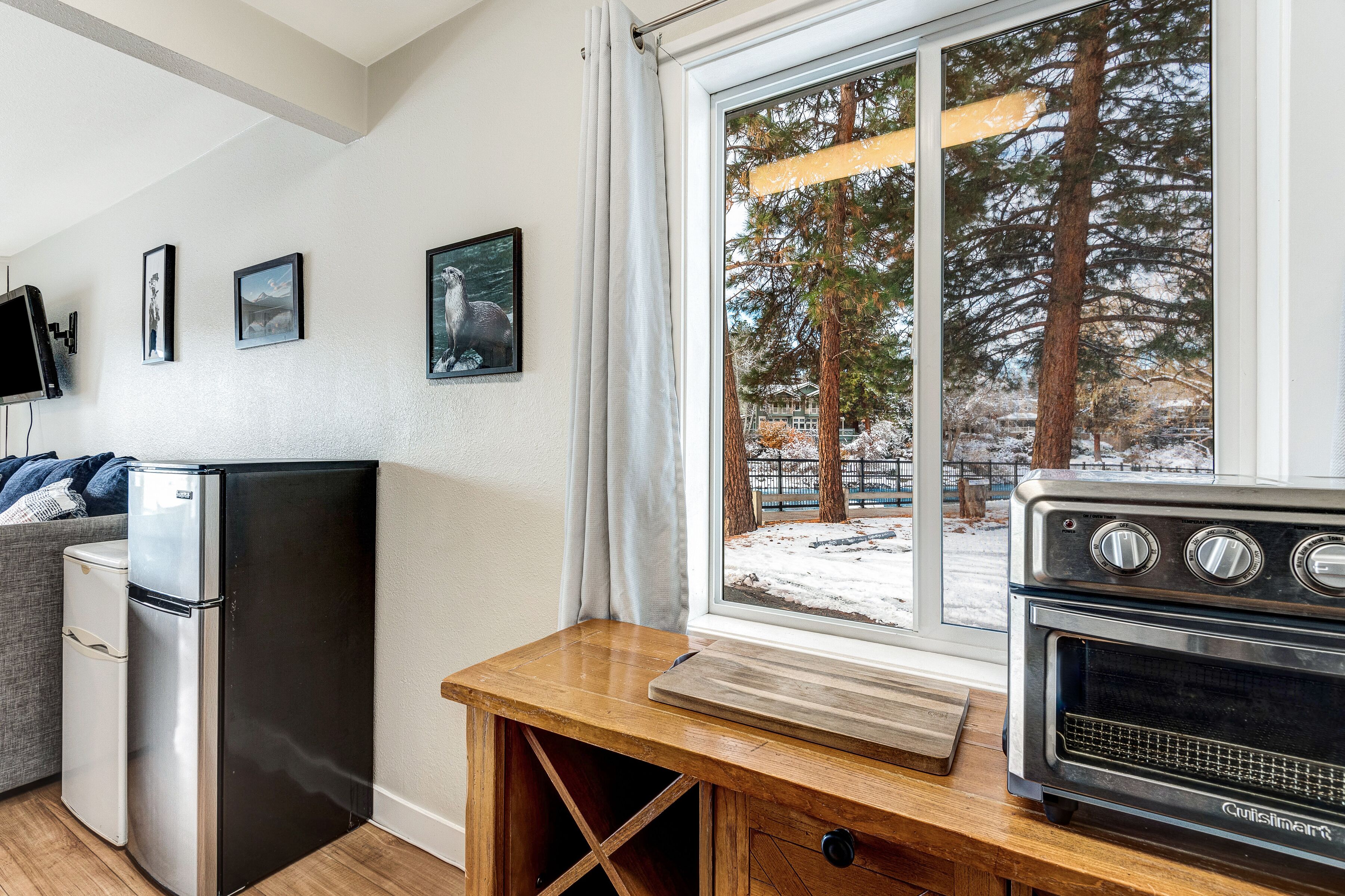 A compact kitchen with a refrigerator, oven, and a window with a view of trees and snow.