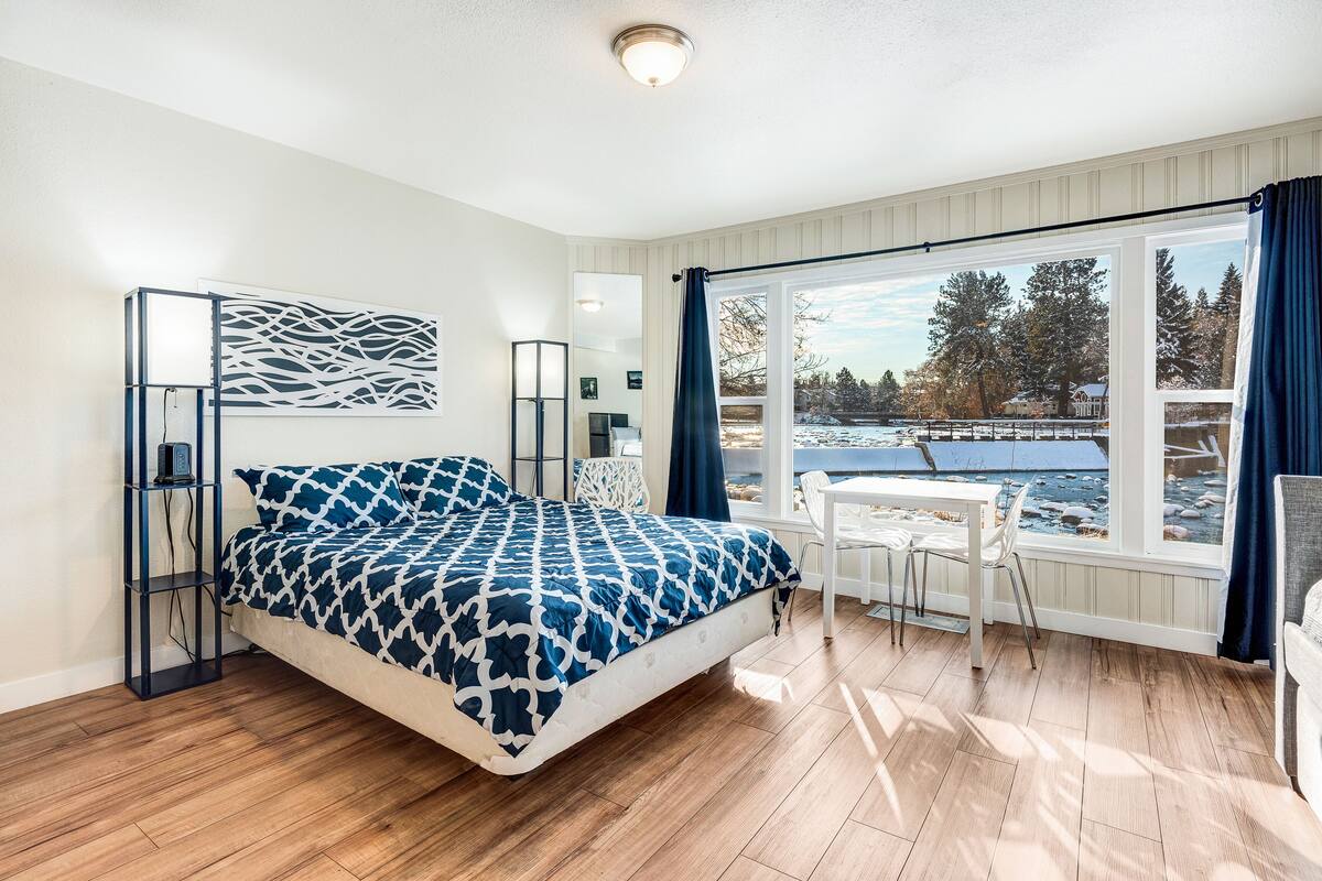 A bedroom with a bed, a desk, and a view of a snowy landscape through large windows.