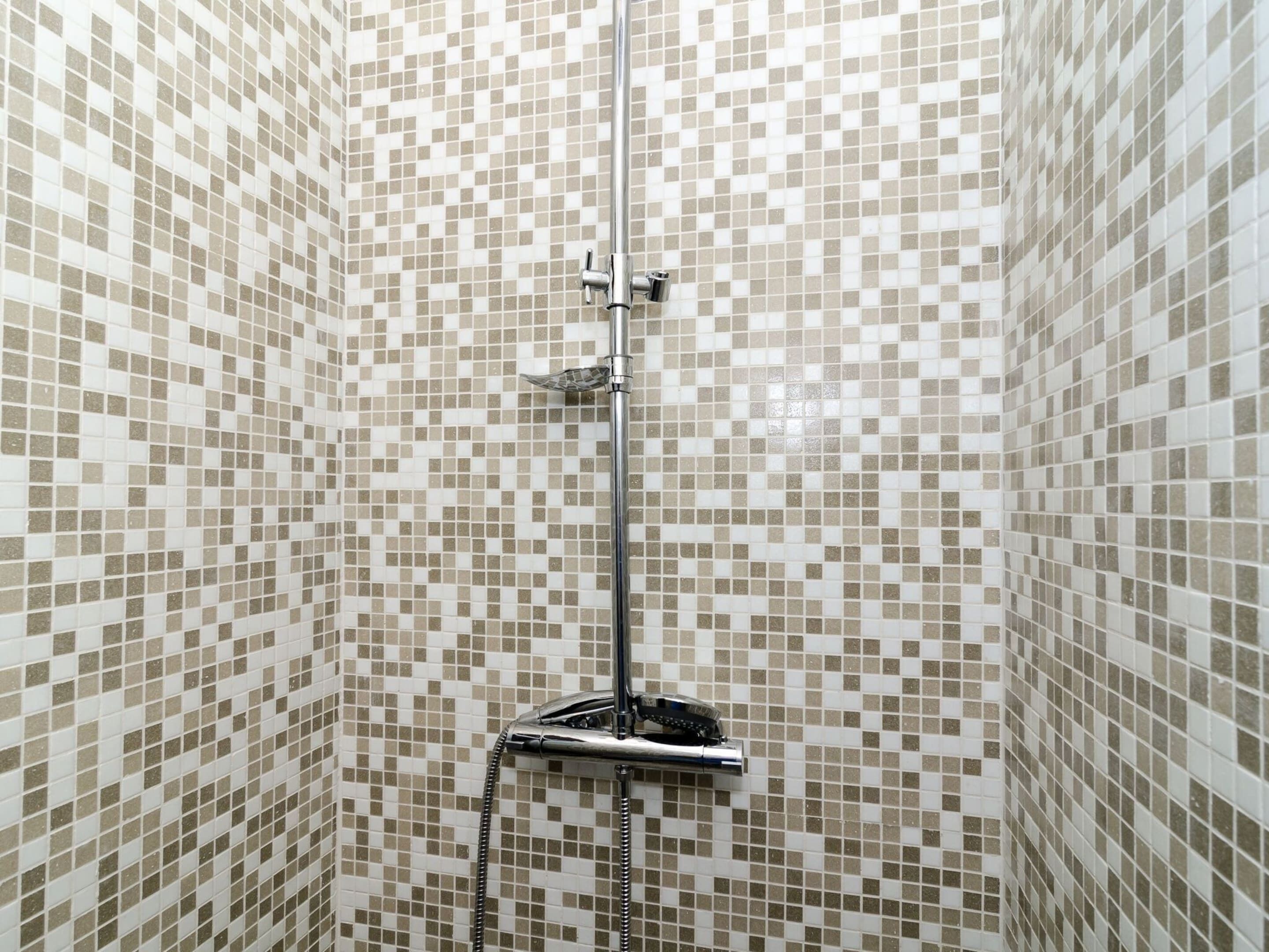 A shower with a chrome hose and a handheld showerhead, set against a wall with a mosaic tile pattern.