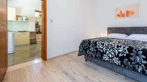 A bedroom with a bed, a wooden floor, a kitchen visible through an open door, and a single wall-mounted light. - Apartments Lucija - One Bedroom Apartment With Terrace (Dubrovnik)