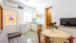 A compact living space with a sofa, dining table, TV, kitchenette, and a small fridge. - Apartments Lucija - One Bedroom Apartment With Terrace (Dubrovnik)
