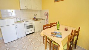 A compact kitchen with white cabinets, a tiled backsplash, a dining table with chairs, and a small refrigerator. - Apartments Bacic - One Bedroom Apartment With Terrace and Sea View (Blato)