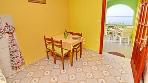 A dining area with a table and chairs, a tiled floor, and a view of the sea through an open door. - Apartments Bacic - One Bedroom Apartment With Terrace and Sea View (Blato)