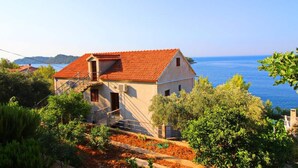 A coastal house with a red-tiled roof, surrounded by lush greenery and overlooking the sea. - Apartments Bacic - One Bedroom Apartment With Terrace and Sea View (Blato)