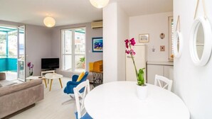 A modern living room with a sofa, a TV, a dining table, and chairs. There is a balcony visible through the window. - Apartment Radovan - One-bedroom Apartment With Balcony and Sea View (Dubrovnik)