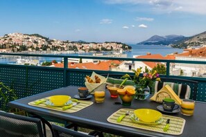 A table set with breakfast items, a view of a coastal town, and a mountain in the distance.