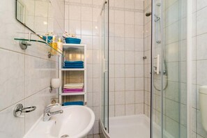 A bathroom with a sink, a glass-enclosed shower, and shelves with folded towels.