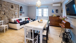 A modern living room with a stone wall, a white sofa with black cushions, a dining table with chairs, and a wooden cabinet. - Villa Nives - Three-bedroom Villa With Terrace and Sea View (Ston)