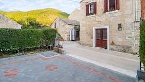 A stone building with a wooden door and windows, surrounded by a paved area with hexagonal tiles and a hedge. - Villa Nives - Three-bedroom Villa With Terrace and Sea View (Ston)
