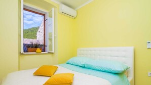 A bedroom with a bed, two pillows, a window with a view of a hill, and an air conditioning unit. - Villa Nives - Three-bedroom Villa With Terrace and Sea View (Ston)