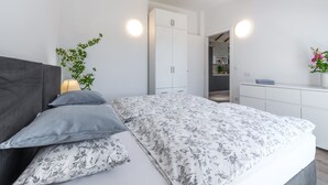 A bedroom with a bed, bedside table, lamp, and a potted plant. - Apartments Terra - Comfort One Bedroom Apartment With Balcony and City View (Dubrovnik)