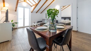 A modern dining area with a wooden table, black chairs, and a vase of green flowers. - Apartments Terra - Comfort One Bedroom Apartment With Balcony and City View (Dubrovnik)