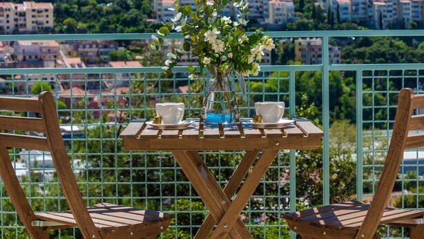 A balcony with a table set for two, featuring a vase with flowers, two cups, and a teapot. - Apartments Terra - Comfort One Bedroom Apartment With Balcony and City View (Dubrovnik)