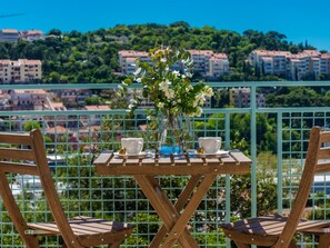 A balcony with a table set for two, featuring a vase with flowers, two cups, and a teapot. - Apartments Terra - Comfort One Bedroom Apartment With Balcony and City View (Dubrovnik)