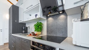 A modern kitchen with dark cabinetry, a built-in oven, and a countertop with a plant. - Apartments Terra - Comfort One Bedroom Apartment With Balcony and City View (Dubrovnik)