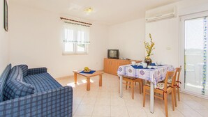 Uma sala de estar com sofá, mesa de jantar com cadeiras, televisão e janela com cortinas.