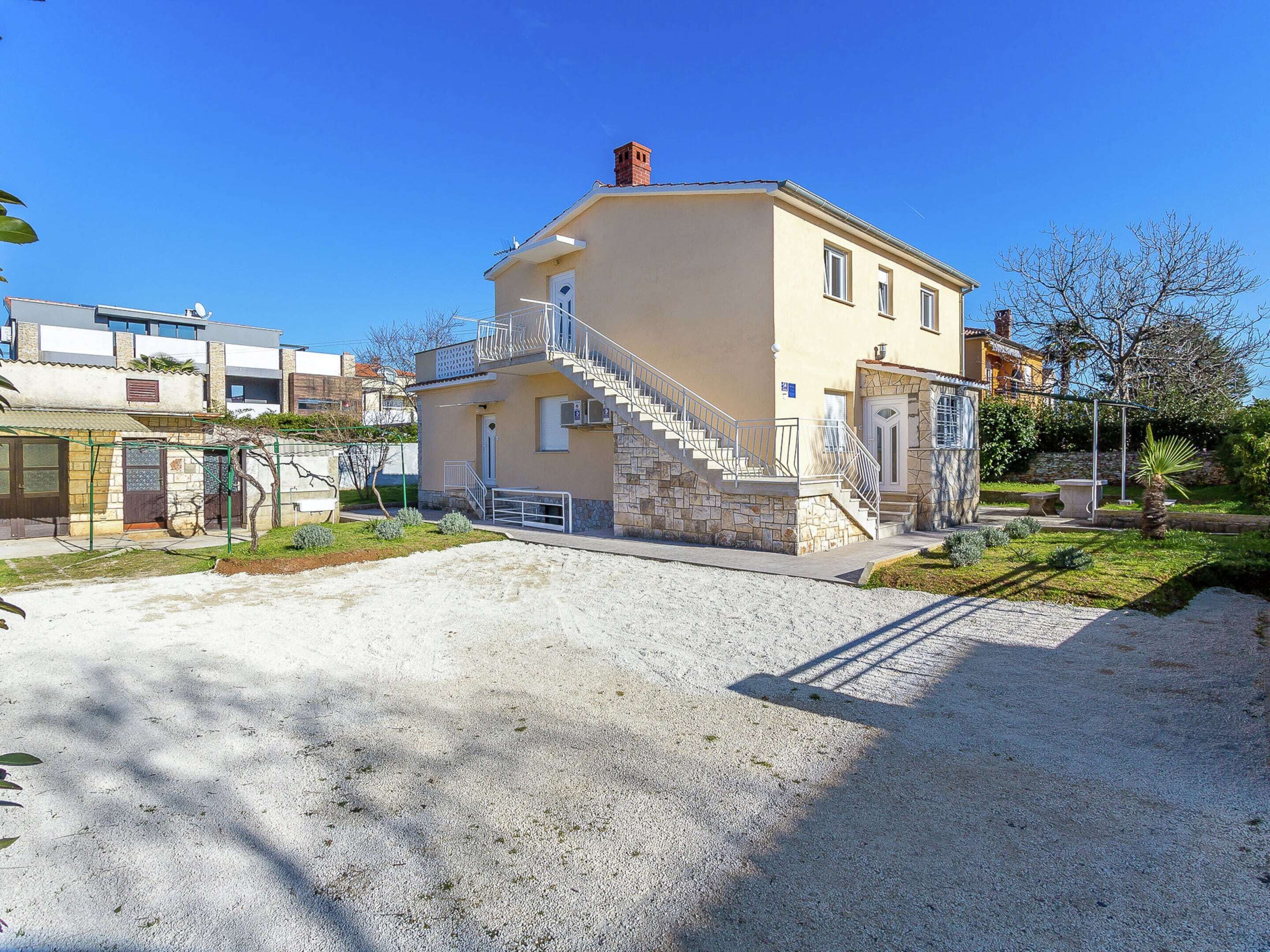 A two-story building with a stone staircase leading to the entrance, surrounded by a gravel driveway and greenery.