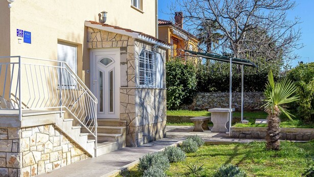 A building with a stone facade, a gated entrance, and a small garden with a palm tree and shrubs. - Apartment With Terrace and Pet-friendly (Medulin)