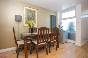 Un coin repas avec une table et des chaises en bois, une œuvre d’art encadrée au mur et une fenêtre donnant sur un paysage.