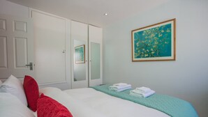 A neatly made bed with white and red pillows, a teal bedspread, and a framed painting of flowers on the wall. - Stunning 3 Bedroom House With Garden in Battersea (London)