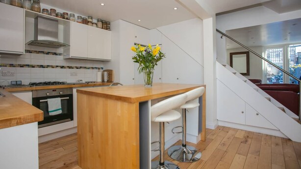 A modern kitchen with a wooden island, white cabinets, and a vase with flowers. - Stunning 3 Bedroom House With Garden in Battersea (London)