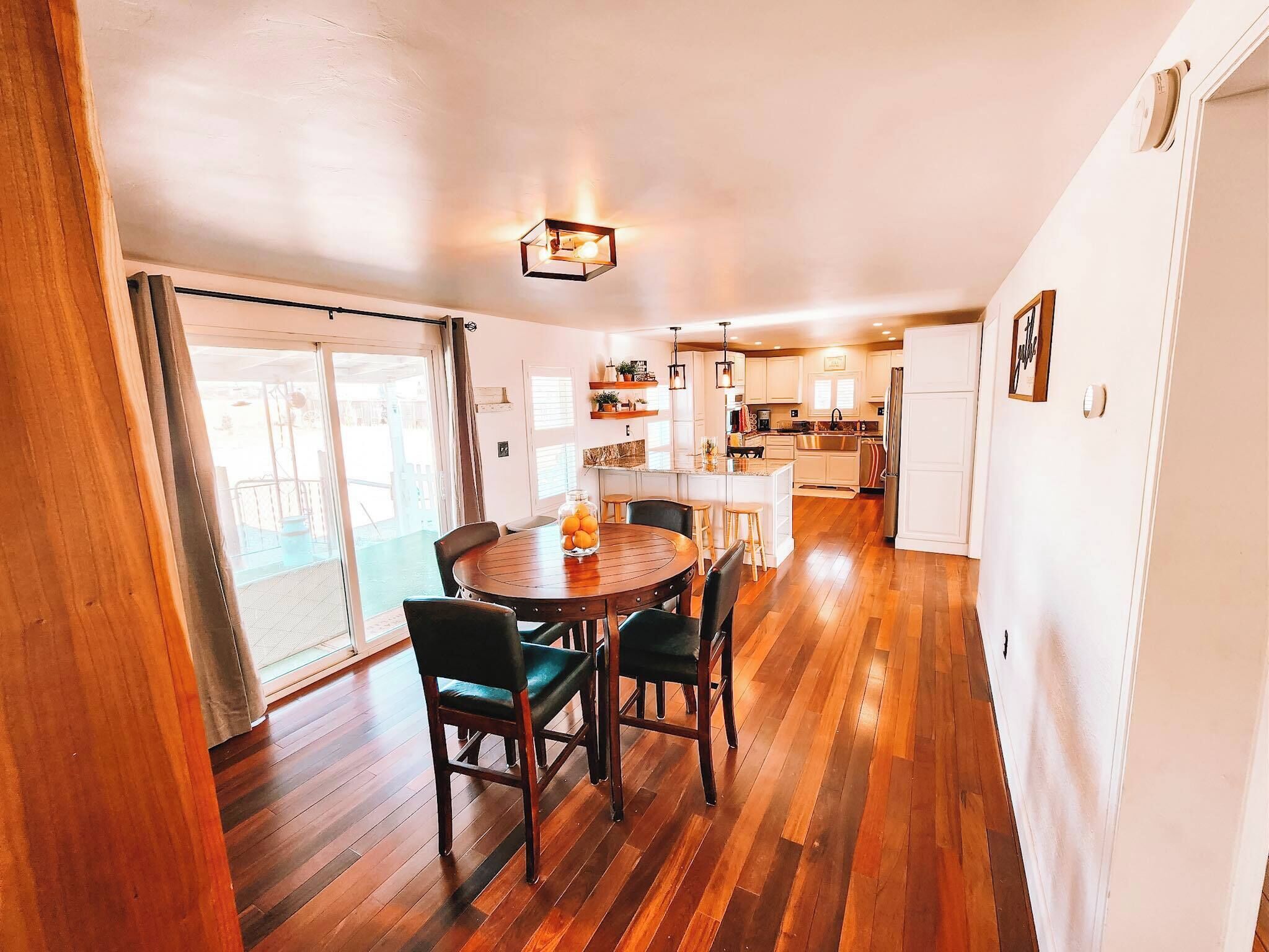 Une cuisine moderne avec un plancher en bois, un coin repas avec une table ronde et des chaises, et une vue sur l’extérieur grâce à de grandes portes coulissantes.