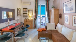 A cozy living room with a sofa, a dining table with chairs, a wooden cabinet, and a large window with curtains. - Apartment in Rome With Balcony (Rome)