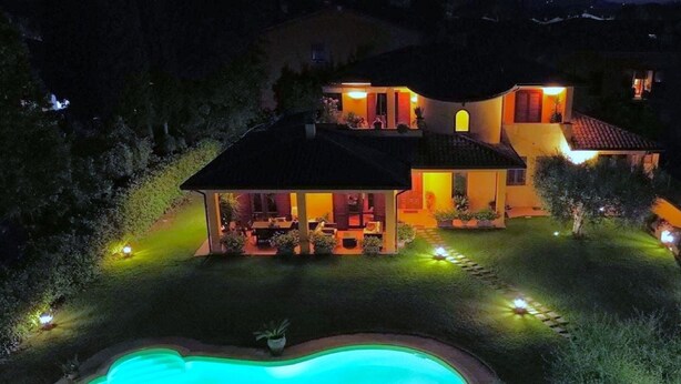 A house with a swimming pool, a patio, and a well-lit garden at night.