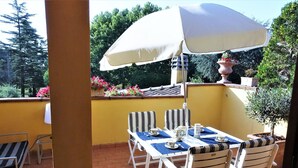 A patio with a table and chairs, a white umbrella, and potted plants.