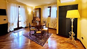 A room with a dining table, chairs, a lamp, and a radiator.