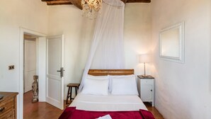 A bedroom with a wooden bed, white bedding, a red throw blanket, a bedside lamp, and a chandelier.