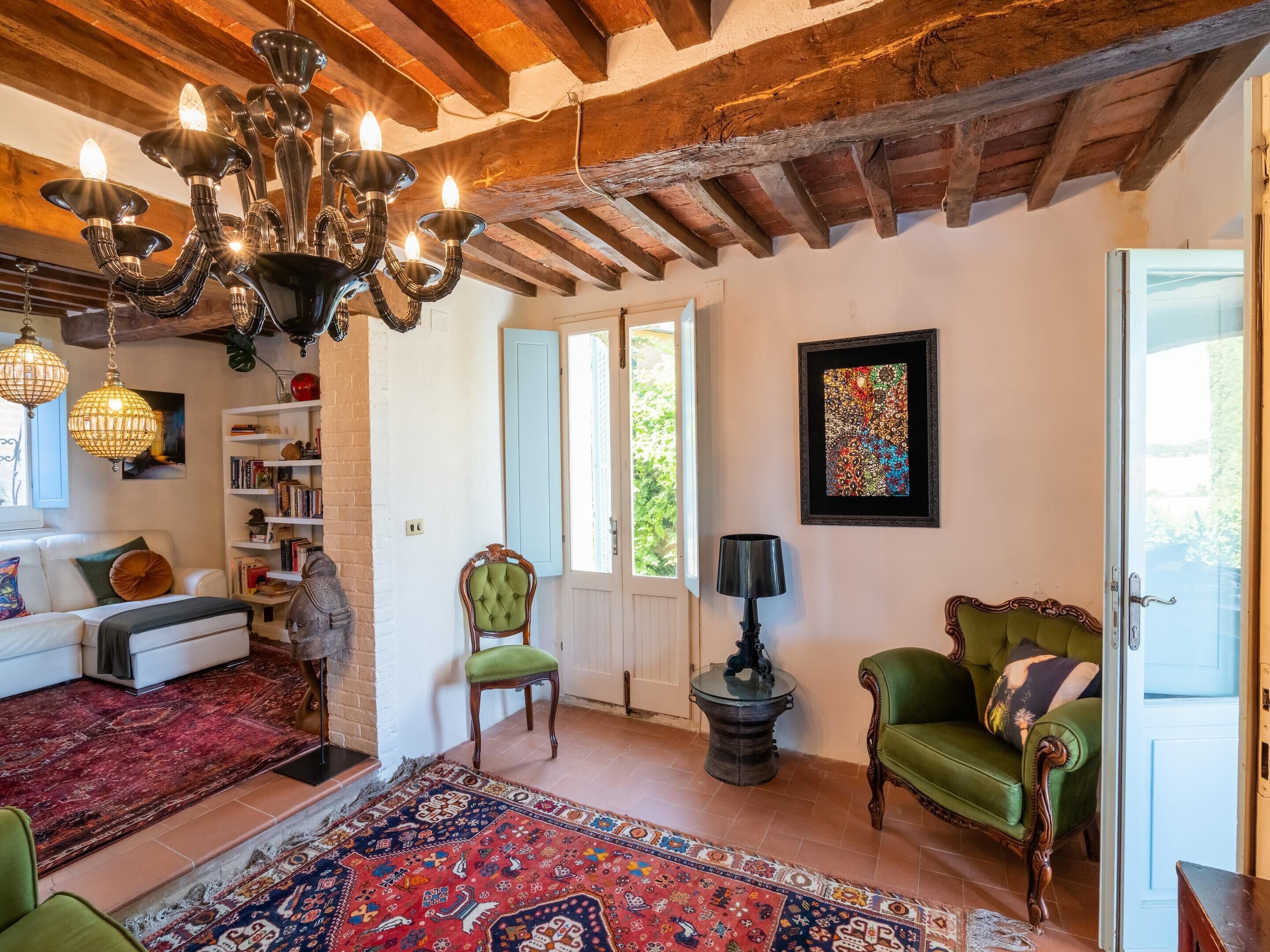 Un salón acogedor con chimenea, un sillón verde, un tapete estampado y una araña.