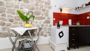 A kitchen with a stone wall, a small table with a white tablecloth, and a white appliance.
