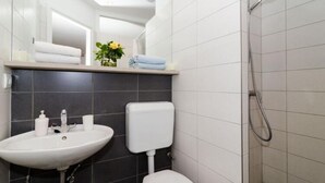 A bathroom with a white sink, dark tiles, a toilet, a shower, and a mirror.