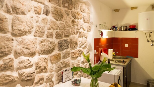 A kitchen with a stone wall, a red backsplash, and a white countertop with a vase of flowers.