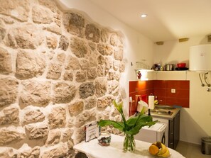 Une cuisine avec un mur en pierre, un pare-feu rouge et un plan de travail blanc agrémenté d’un vase de fleurs.