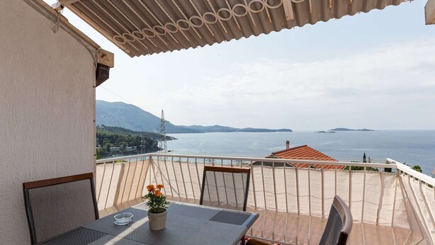 A balcony with a table and chairs, overlooking a body of water and distant land.