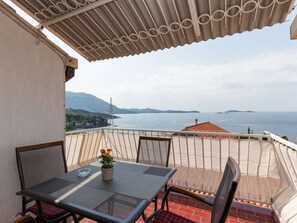 A balcony with a table and chairs, overlooking a body of water and distant land. - Apartments Kisic - Two-bedroom Apartment With Balcony and Sea View (Zupa dubrovacka)