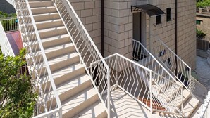 A building with a staircase leading to an entrance, a sign indicating "Apartments KISIC," and a clear sky in the background.