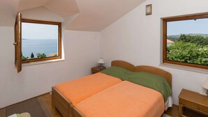 A bedroom with a bed, two windows, a nightstand, and a view of the sea.