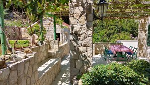 A stone pathway leading to a stone building with a wooden pergola and a table with chairs covered by a checkered tablecloth. - Guest House Hazdovac Rooms - Two Bedroom Apartment With Terrace and Sea View (Mljet)