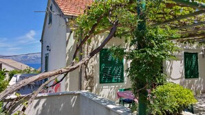 A white building with a red-tiled roof, green shutters, and a vine-covered wall. - Guest House Hazdovac Rooms - Two Bedroom Apartment With Terrace and Sea View (Mljet)