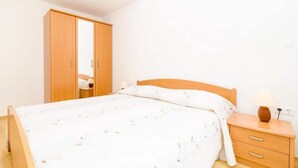 A bedroom with a bed, wooden wardrobe, bedside table, and lamp. - Apartments Nikola - One Bedroom Apartment With two Balconies and Sea View (Dubrovnik)
