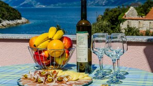 A table with a bottle of wine, glasses, a fruit bowl, and a plate of food. - Apartment Bay Of Dreams - Two-bedroom Apartment With Terrace and Sea View (Janjina)