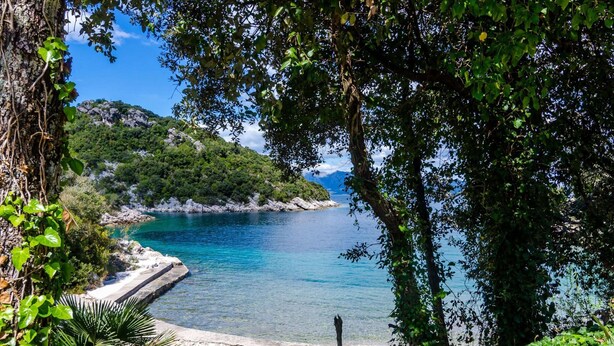 A coastal landscape with a pebble beach, clear blue water, and lush greenery. - Apartment Bay Of Dreams - Two-bedroom Apartment With Terrace and Sea View (Janjina)