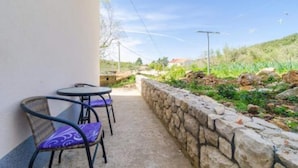 A balcony with two chairs and a table, a stone wall, and a view of a green landscape. - Apartments Dalamar - Studio With Terrace (Mljet)