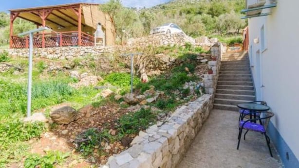 A hillside property with a stone retaining wall, a wooden pergola, and a staircase leading to a white building. - Apartments Dalamar - Studio With Terrace (Mljet)